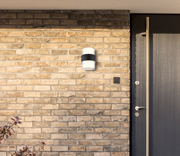 LED-Außenwandleuchte an einer Ziegelwand neben einer Haustür, seitliche Perspektive