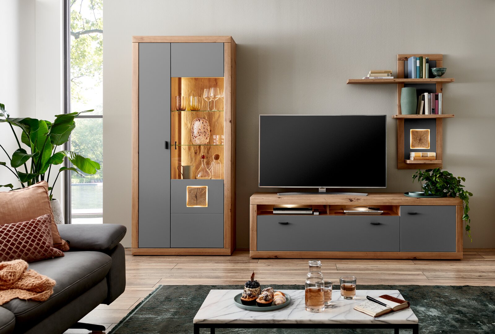 Moderne wandcombinatie in houtlook met grijze fronten, bestaande uit een vitrinekast, een tv-meubel en een wandrek, hier afgebeeld in vooraanzicht.