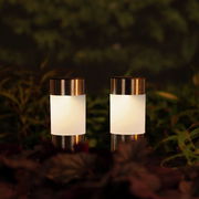 Zwei Solar Stabbeleuchten aus Edelstahl in einem Garten, frontal fotografiert, umgeben von Pflanzen.