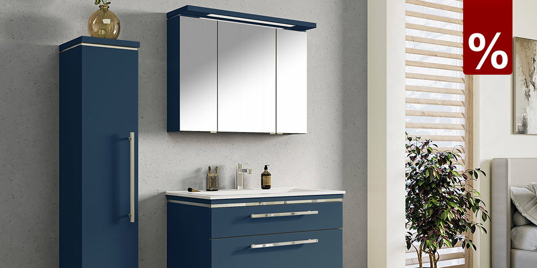 Moderne badkamer met een zwevende badmeubelset in mat donkerblauw, een witte wastafel, een driedeurs spiegelkast met LED-verlichting en een bijpassende hoge kast tegen een wand in lichte betonlook.