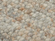 Nahaufnahme eines handgewebten Teppichs mit einer texturierten Oberfläche aus dicken, weichen Wollknäueln in natürlichen Beige- und Grautönen.