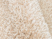 Nahaufnahme eines beigen Hochflor-Teppichs mit weicher, flauschiger Textur.