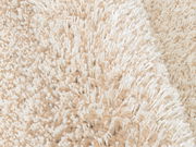 Nahaufnahme eines beigen Hochflor-Teppichs mit weicher, flauschiger Textur.