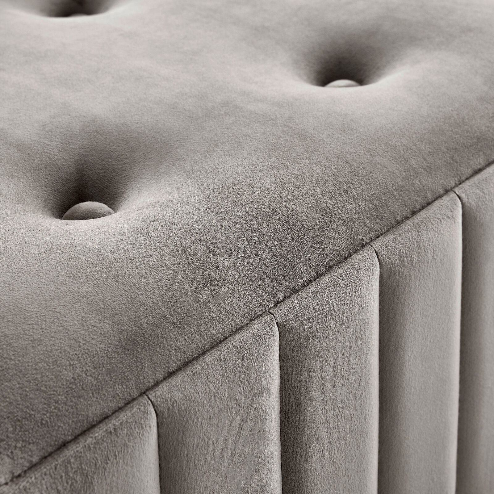 Nahaufnahme einer grauen Hockerbank mit gepolstertem, gestepptem Design und vertikalen Nähten, seitliche Perspektive