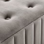 Nahaufnahme einer grauen Hockerbank mit gepolstertem, gestepptem Design und vertikalen Nähten, seitliche Perspektive