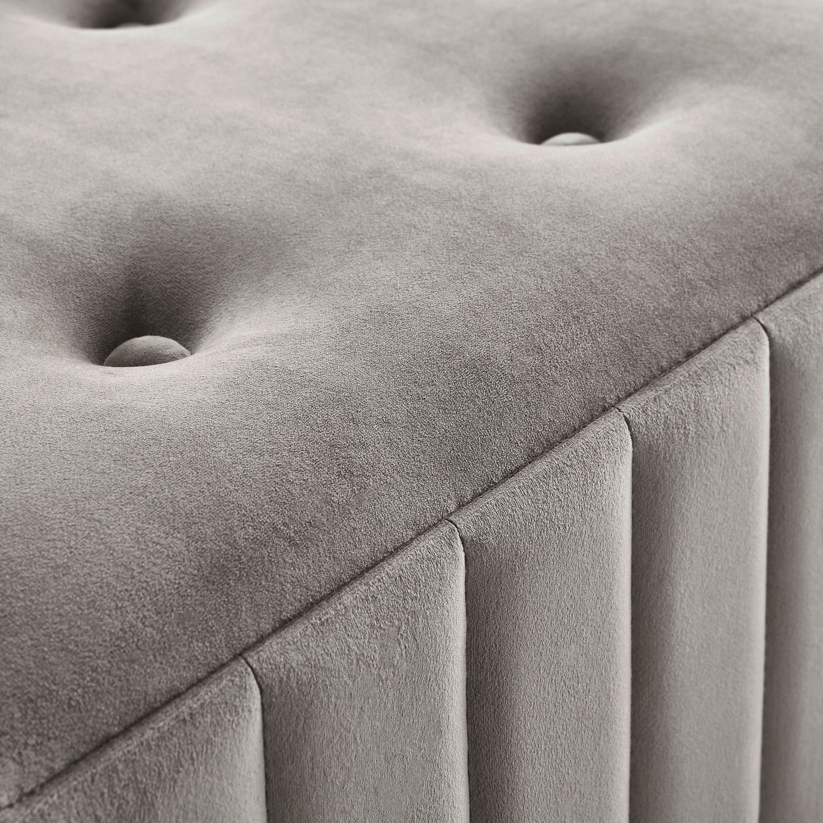 Nahaufnahme einer grauen Hockerbank mit gepolstertem, gestepptem Design und vertikalen Nähten, seitliche Perspektive