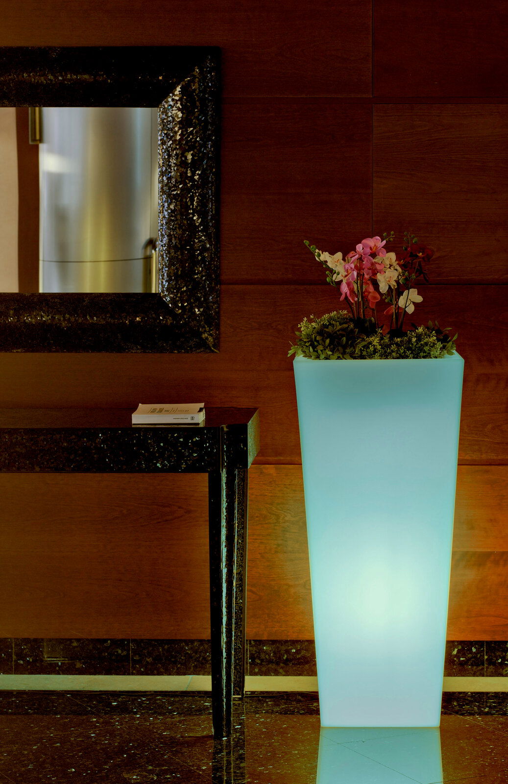 Hoher, leuchtender Blumentopf Melisa 50 mit Orchideen und Grünpflanzen, seitliche Perspektive.