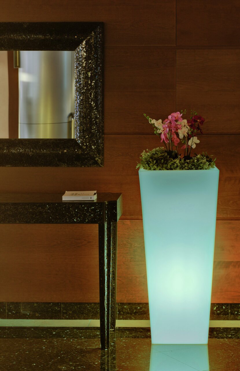 Hoher, leuchtender Blumentopf Melisa 50 mit Orchideen und Grünpflanzen, seitliche Perspektive.