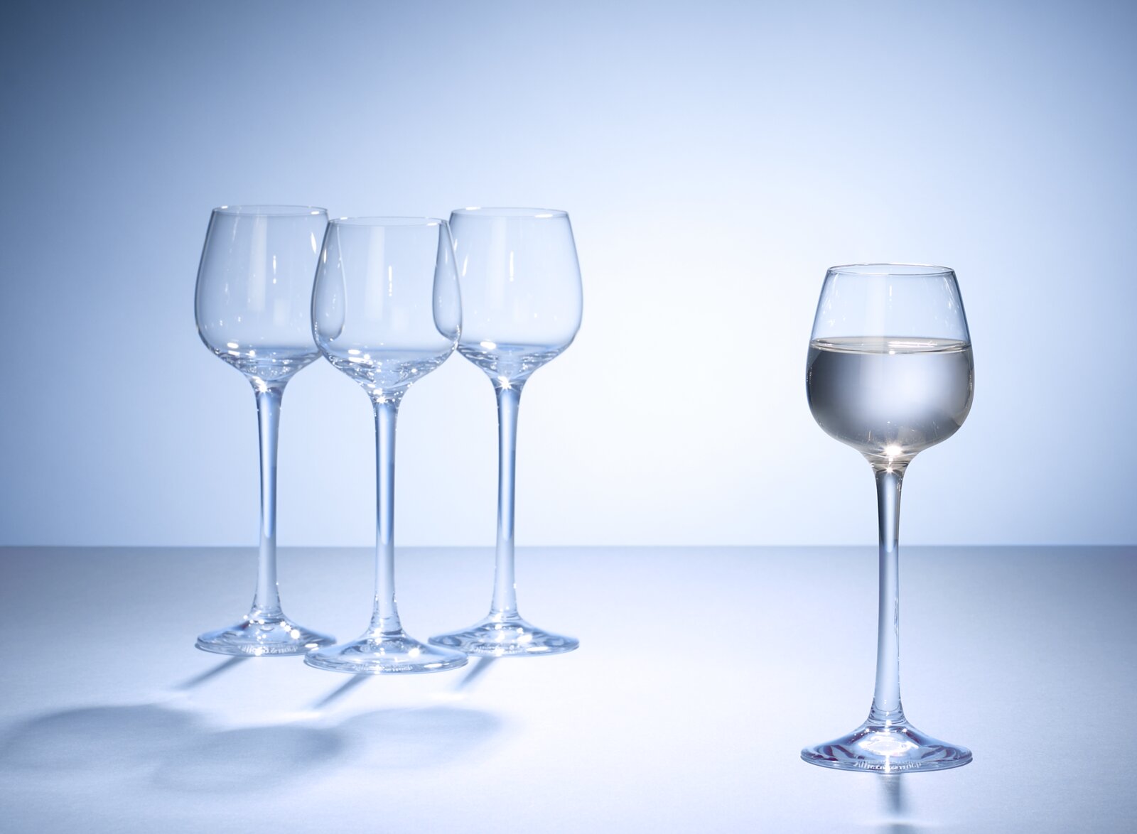Vier elegante Grappagläser, eines davon gefüllt, aus seitlicher Perspektive fotografiert.