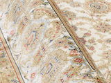 Nahaufnahme eines Orientteppichs mit floralen Mustern in Beige, Rot und Blau. Der Teppich ist teilweise aufgerollt, was die Textur und Details des Musters hervorhebt.