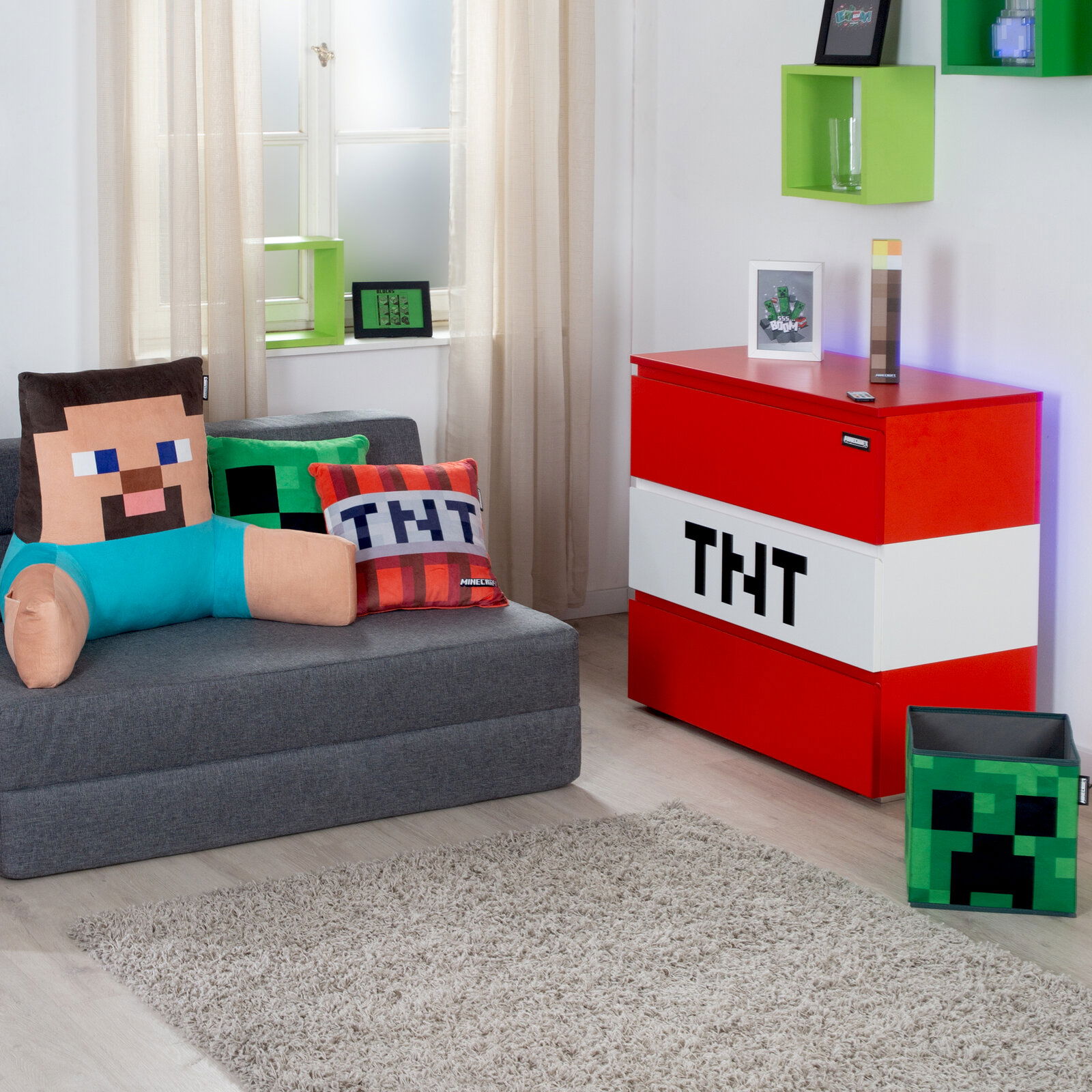 Minecraft-inspiriertes Kinderzimmer-Setup mit roter TNT-Aufbewahrungsbox/Truhe und grauem Sofa mit Pixel-Kissen; Perspektive: frontale, leicht seitliche Raumansicht.