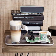 Latte Macchiato Glas 0,3l mit Edelstahlgriff, gefüllt mit geschichtetem Kaffee und Milchschaum, auf einem Tablett neben einer Espressotasse, seitliche Perspektive