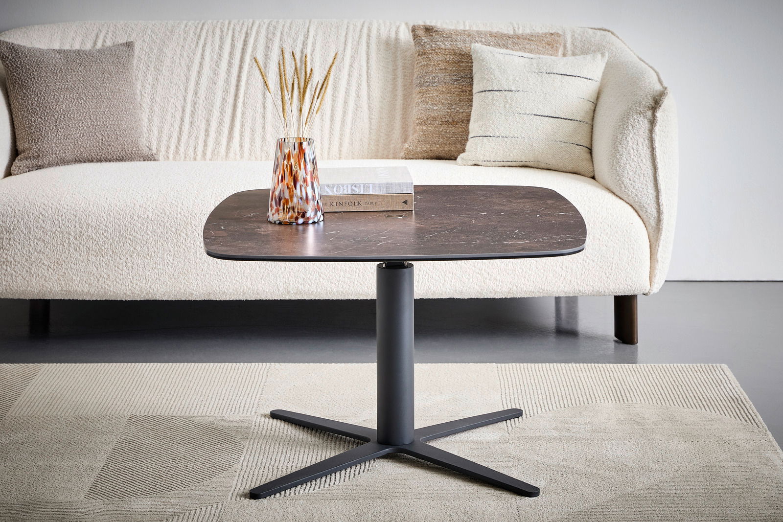 Moderner Couchtisch mit dunkler Tischplatte und schwarzem Metallfuß, frontal vor einem cremefarbenen Sofa mit Kissen.