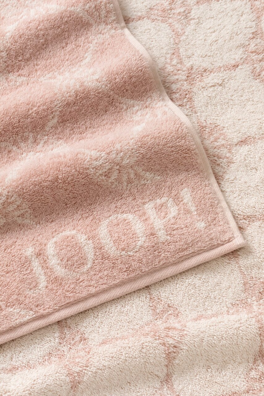 Nahaufnahme eines weichen, rosa Gästetuchs mit eingewebtem Muster und dem Schriftzug 'JOOP!' in der Ecke.