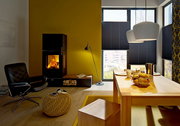 Gemütliches Wohnzimmer mit modernem Kamin, gelber Wand, schwarzem Sessel und Esstisch mit Frühstück, aus der Perspektive eines Betrachters im Raum.