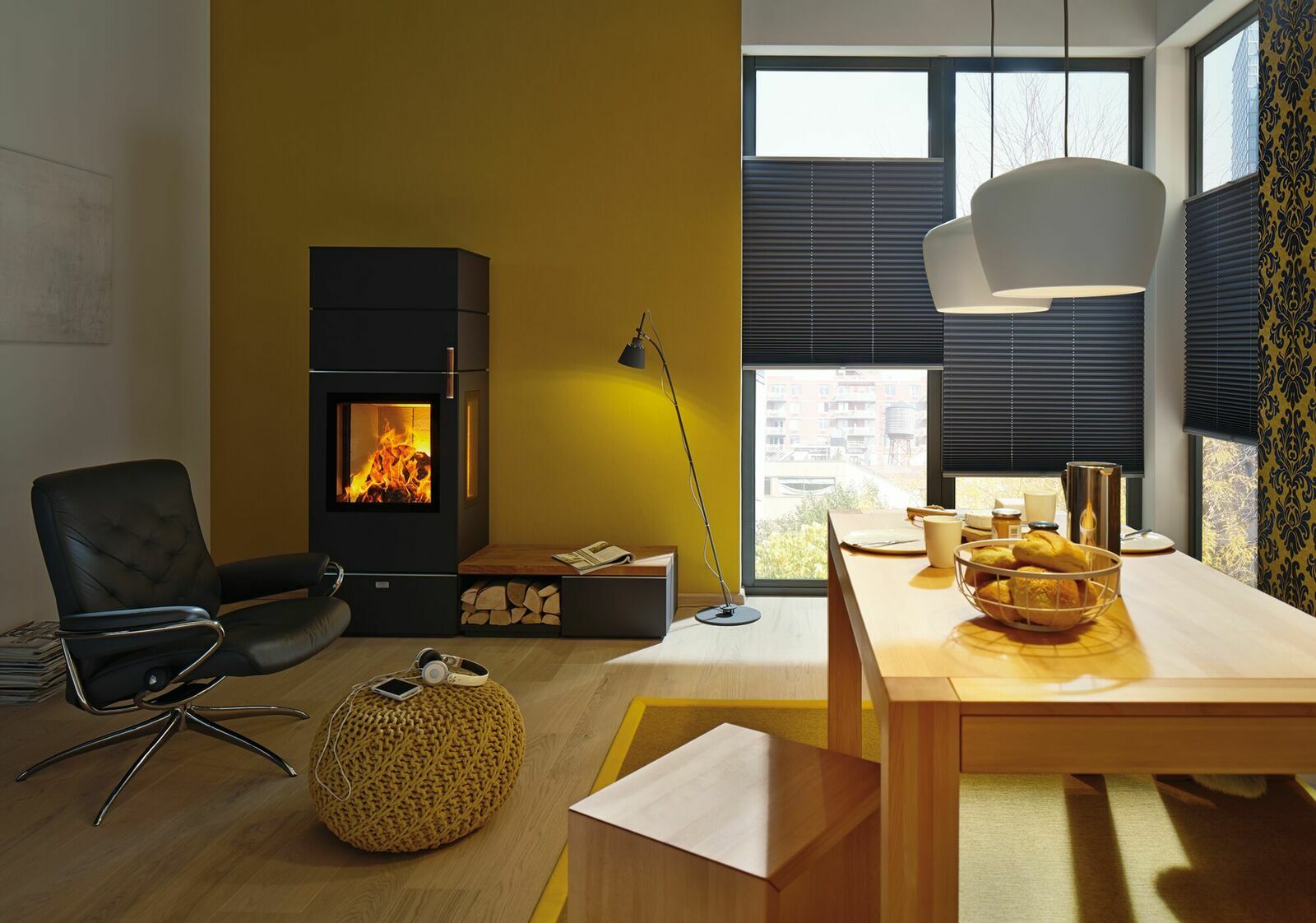 Gemütliches Wohnzimmer mit modernem Kamin, gelber Wand, schwarzem Sessel und Esstisch mit Frühstück, aus der Perspektive eines Betrachters im Raum.