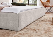 Modernes Polsterbett in hellem Beige mit breitem, weich gerundetem Bettrahmen, aus niedriger Perspektive schräg von vorne im stilvollen Schlafzimmer gezeigt