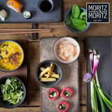 Vogelperspektive auf ein Set von vier anthrazitfarbenen Dip-Schalen, gefüllt mit verschiedenen Zutaten wie Sushi, Minze, Babymais und Ingwer, auf einem Holztisch arrangiert.