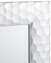 Nahaufnahme eines Spiegels mit facettiertem, sechseckigem Rahmen in silberner Optik, perspektivisch von der Ecke aus gesehen.