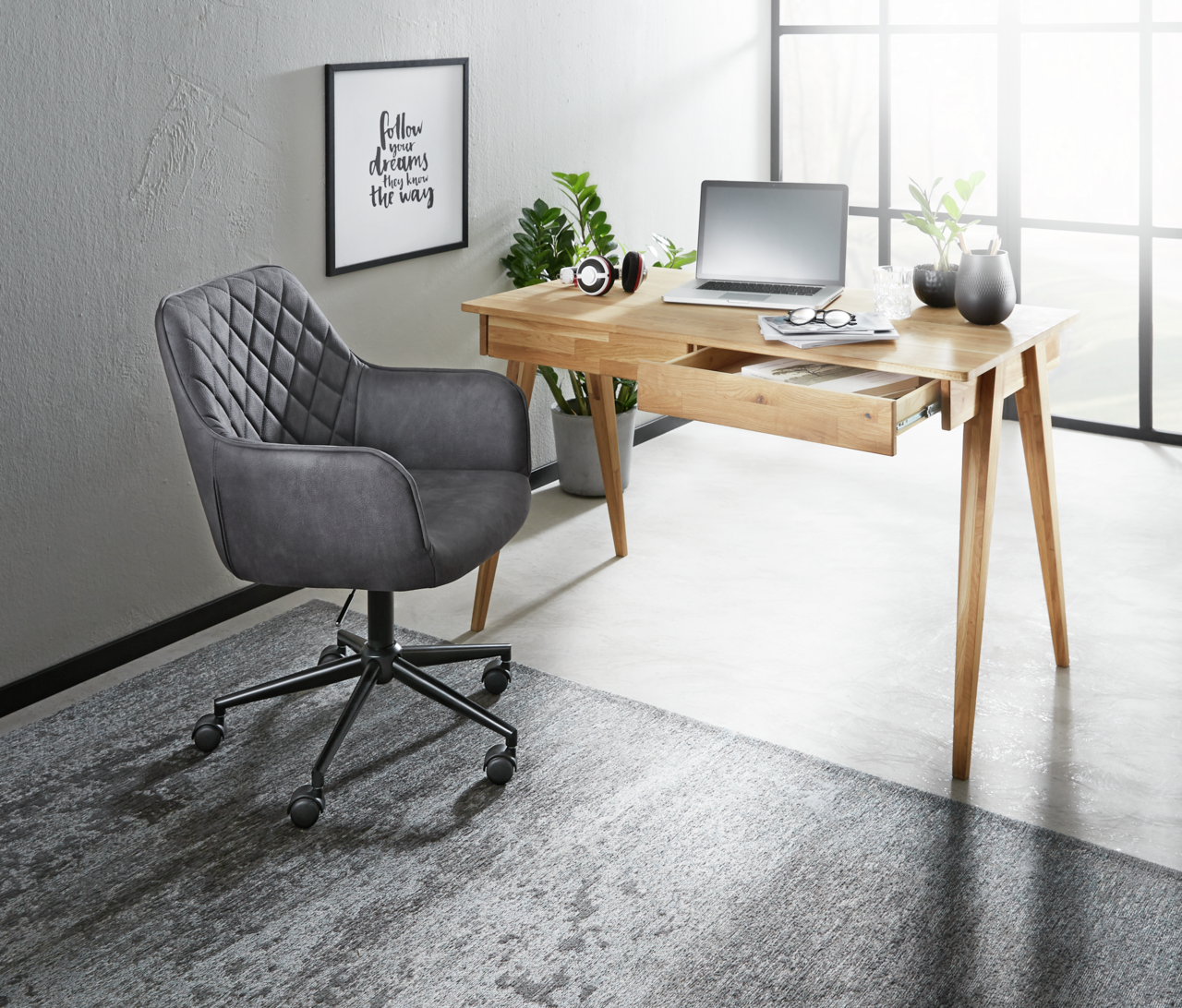 XORA Drehstuhl MARTHA Grauer Drehstuhl mit gesteppter Rückenlehne, seitliche Perspektive, neben einem Holztisch in einem modernen Büro.