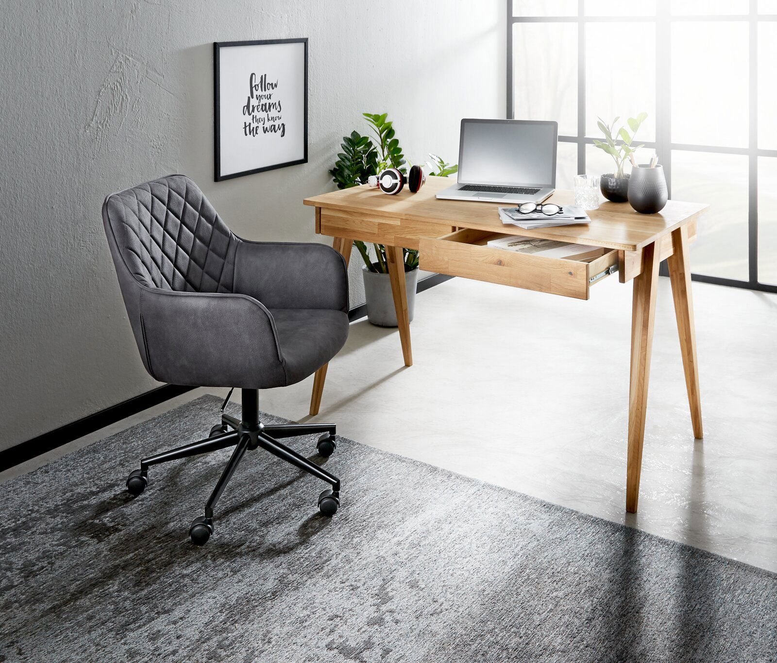 Grauer Drehstuhl mit gesteppter Rückenlehne, seitliche Perspektive, neben einem Holztisch in einem modernen Büro.