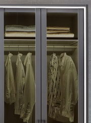 Nahaufnahme eines Drehtürenschranks mit sechs Türen, teilweise geöffnet, mit sichtbaren Regalen und hängender Kleidung.