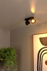 Deckenstrahler in modernem Design, von unten fotografiert, beleuchtet einen Raum mit einem Kunstwerk und einer Pflanze.