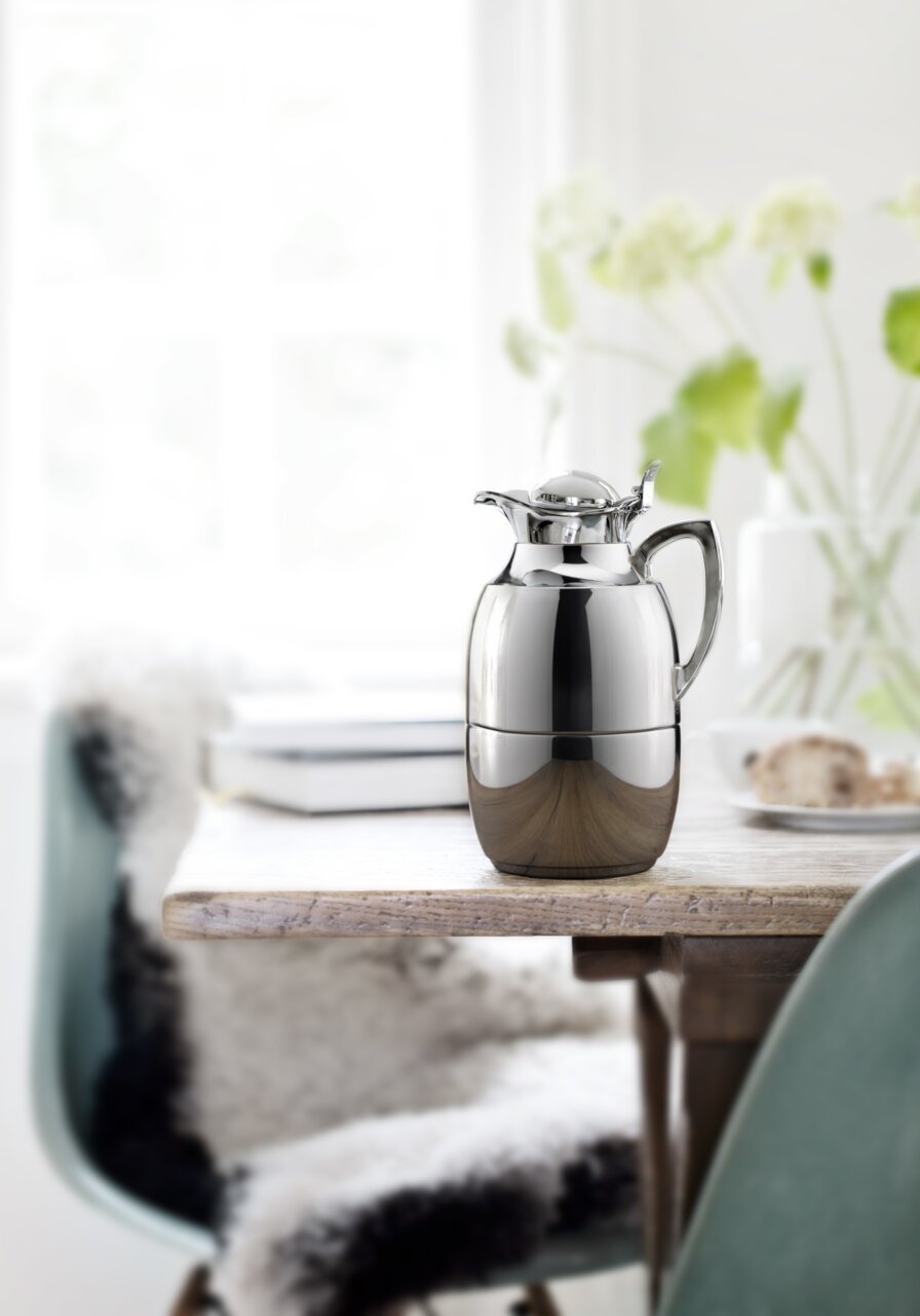 Elegante Isolierkanne Juwel aus Edelstahl auf einem Tisch, seitliche Perspektive.