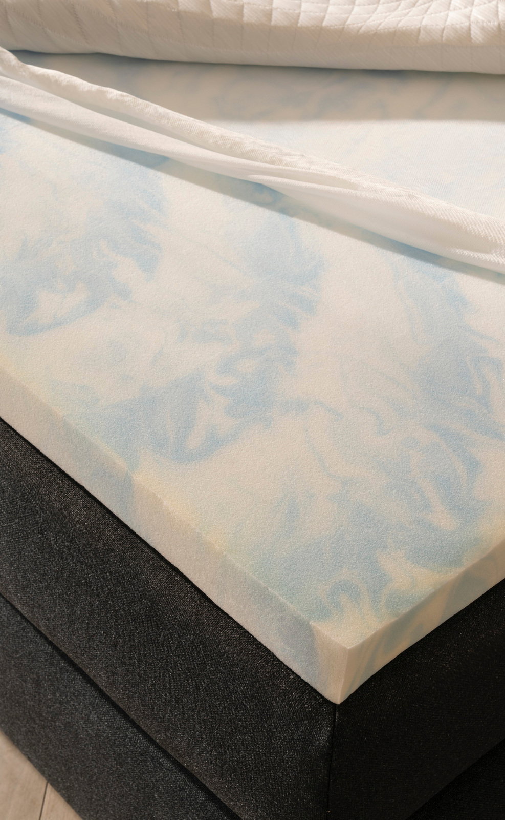 Nahaufnahme eines Boxspringbetts mit einer Schicht aus hellblauem Schaumstoff und einem weißen Bezug, von oben betrachtet.