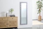 Rechteckiger Spiegel mit dekorativem Rahmen, an einer weißen Wand hängend, neben einer Kommode und einer Pflanze, aus seitlicher Perspektive.