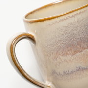 Nahaufnahme einer beigefarbenen Keramik-Kaffeetasse mit braunem Rand und Henkel, seitliche Perspektive vor weißem Hintergrund