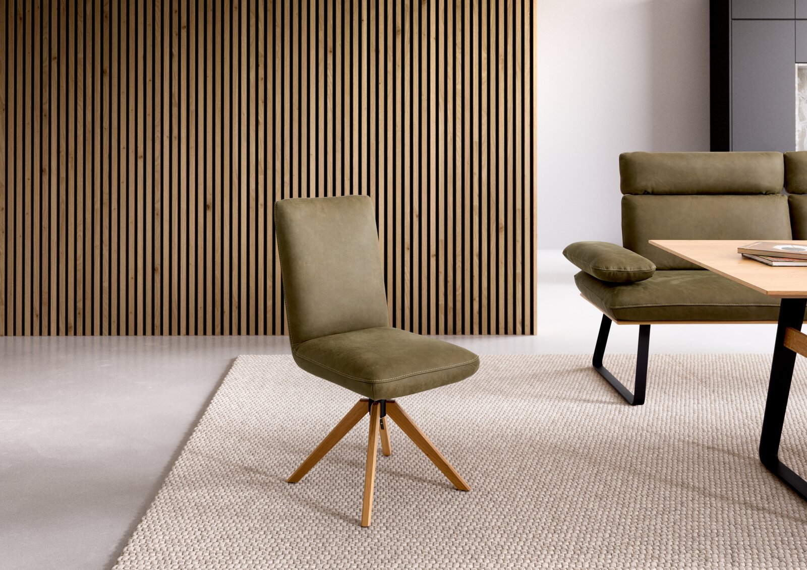 Koinor Stuhl ASCOLIO Olivgrüner Polsterstuhl mit Holz-Drehgestell im modernen Wohnzimmer, frontale Ansicht in leichter Seitenperspektive vor Holzlamellenwand und neben Couchtisch