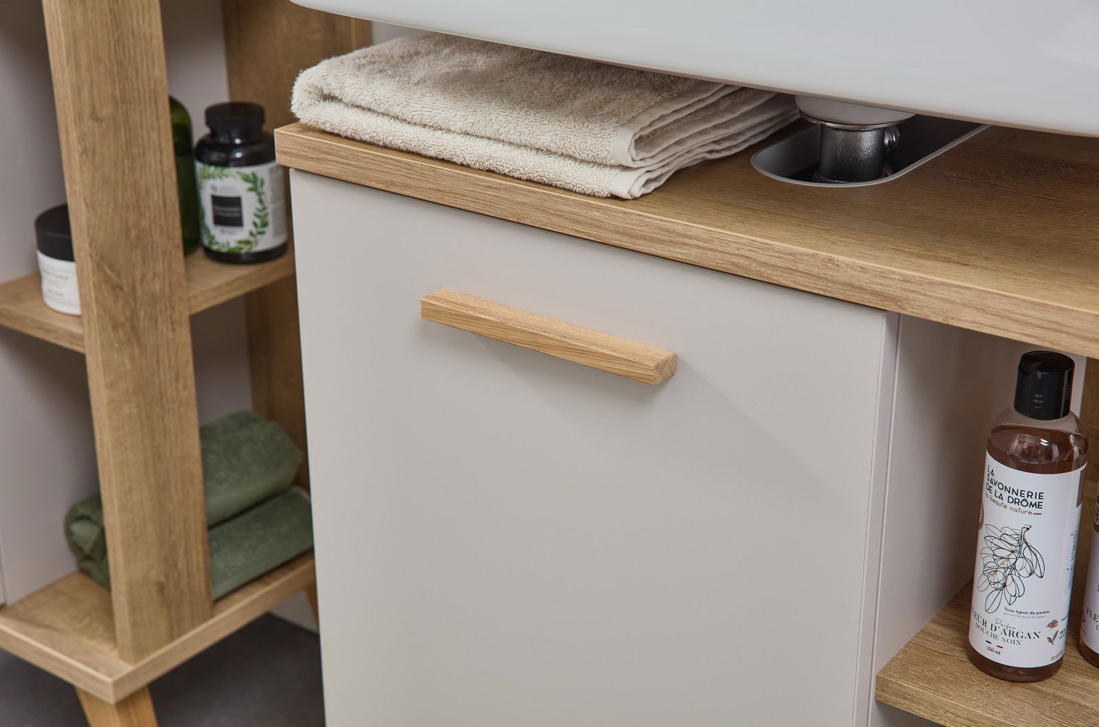 Nahaufnahme eines modernen Waschbeckenunterschranks mit Holzgriff und Ablagefläche, auf der Handtücher liegen. Perspektive von vorne.