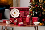 Festlicher Porzellan-Adventskalender in Rot und Gold mit weihnachtlich verziertem Geschirr, frontal aus leicht erhöhter Perspektive vor einem geschmückten Weihnachtsbaum präsentiert.