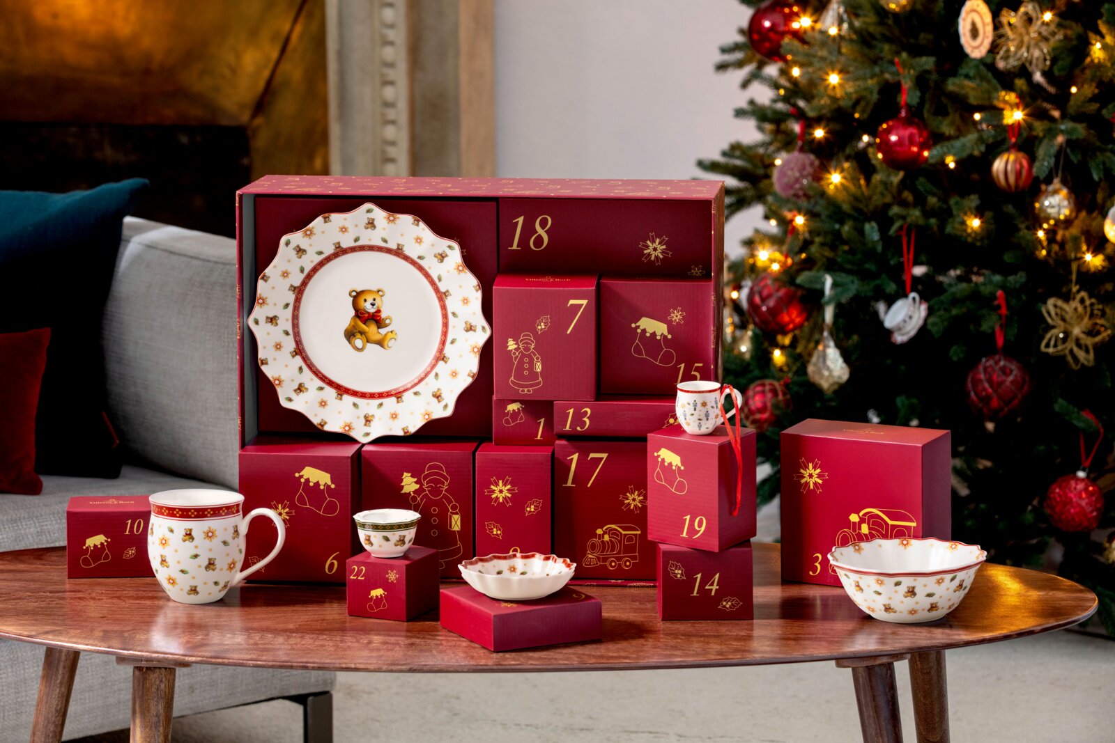 Festlicher Porzellan-Adventskalender in Rot und Gold mit weihnachtlich verziertem Geschirr, frontal aus leicht erhöhter Perspektive vor einem geschmückten Weihnachtsbaum präsentiert.