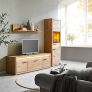 Wohnzimmeransicht mit Cantus Vitrine CLEVELAND, Lowboard und Wandboard aus Holz, beleuchtet, mit Dekorationen und Fernseher, seitliche Perspektive.