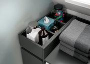 Geöffnete, anthrazitfarbene Schublade im Badezimmer mit geordneten Pflegeartikeln, Taschentuchbox und Handtüchern, aus schräger Draufsicht von oben.