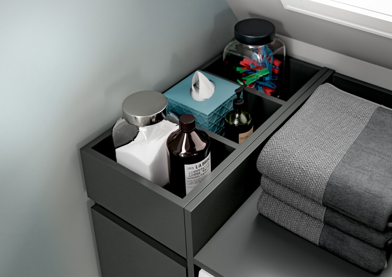Geöffnete, anthrazitfarbene Schublade im Badezimmer mit geordneten Pflegeartikeln, Taschentuchbox und Handtüchern, aus schräger Draufsicht von oben.