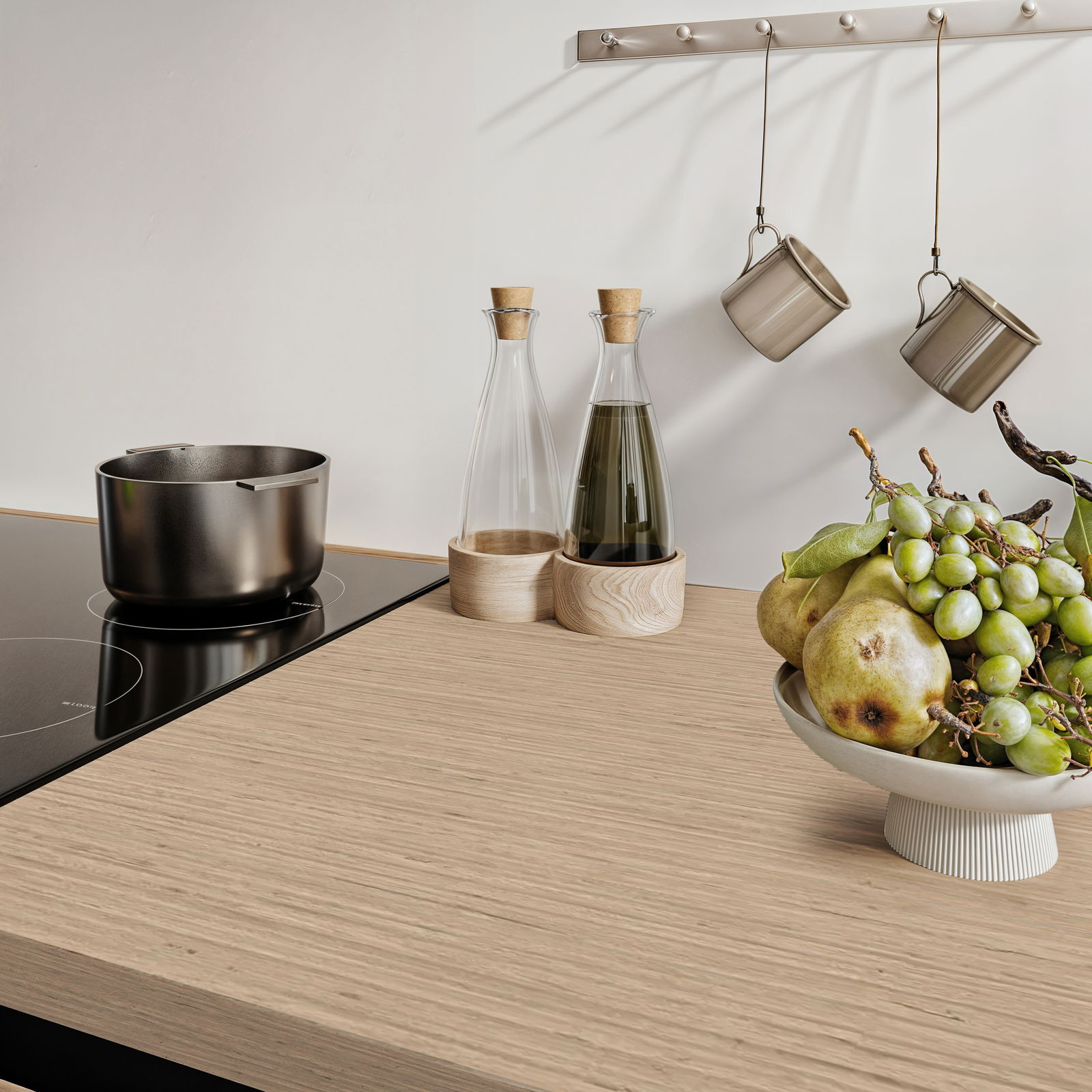 Moderne Küchenarbeitsplatte mit Induktionskochfeld, Topf, Ölflaschen und Obstschale mit Trauben und Birnen, seitliche Perspektive.