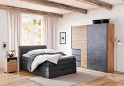 Moderner Schwebetürenschrank in Holz- und Betonoptik, seitliche Perspektive im Schlafzimmer mit Bett und Nachttisch.
