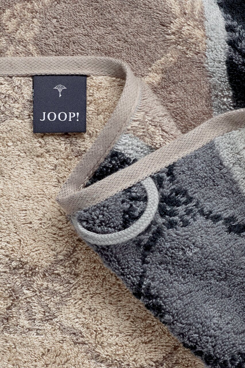 Close-up van een JOOP!-handdoek met een patroon in beige- en grijstinten, inclusief label en ophanglus.