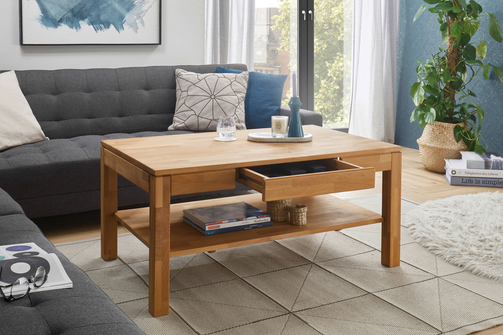 Moderner Couchtisch aus Holz mit Schublade und Ablage, umgeben von einem gemütlichen Wohnzimmer mit Sofa und Pflanzen, aus seitlicher Perspektive.