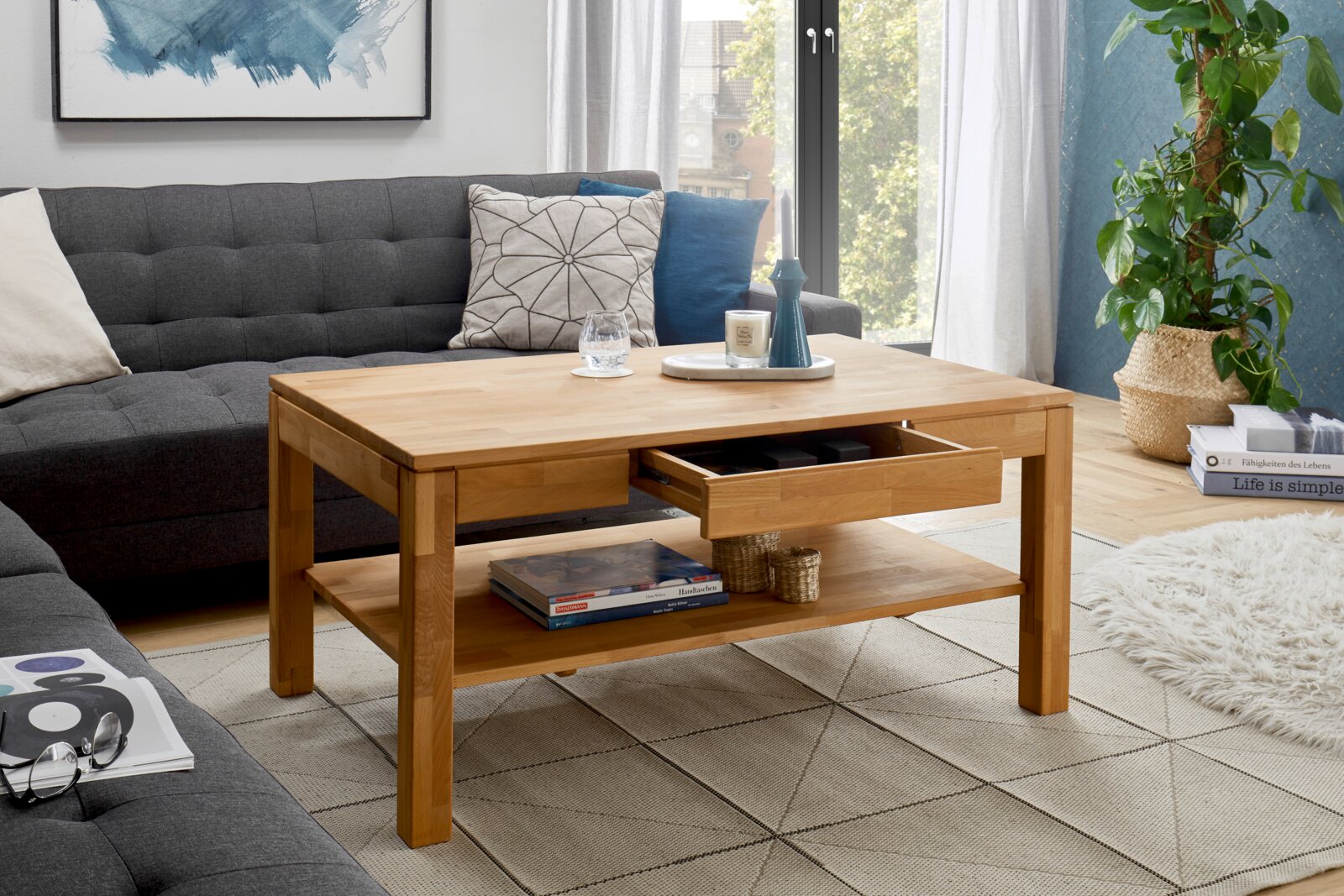 Moderner Couchtisch aus Holz mit Schublade und Ablage, umgeben von einem gemütlichen Wohnzimmer mit Sofa und Pflanzen, aus seitlicher Perspektive.