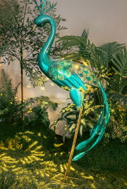 Dekorative Solarleuchte in Form eines Pfaus, seitliche Perspektive, umgeben von Pflanzen.