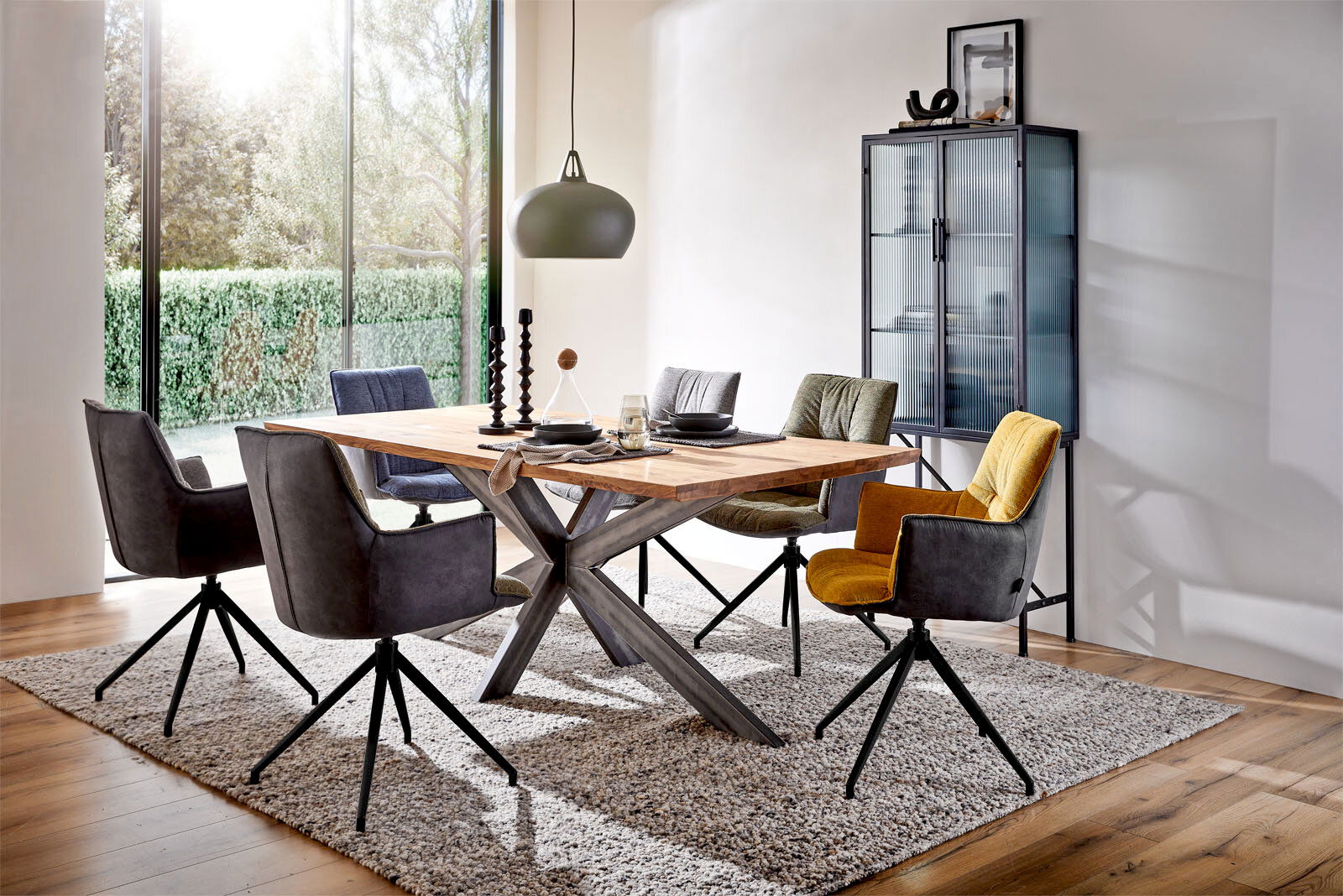 Linea Natura Esstisch SPIDER II Esszimmer mit modernem Esstisch aus Holz und Metallgestell, umgeben von bunten Sesseln auf Teppich, mit Blick auf großen Fensterbereich.