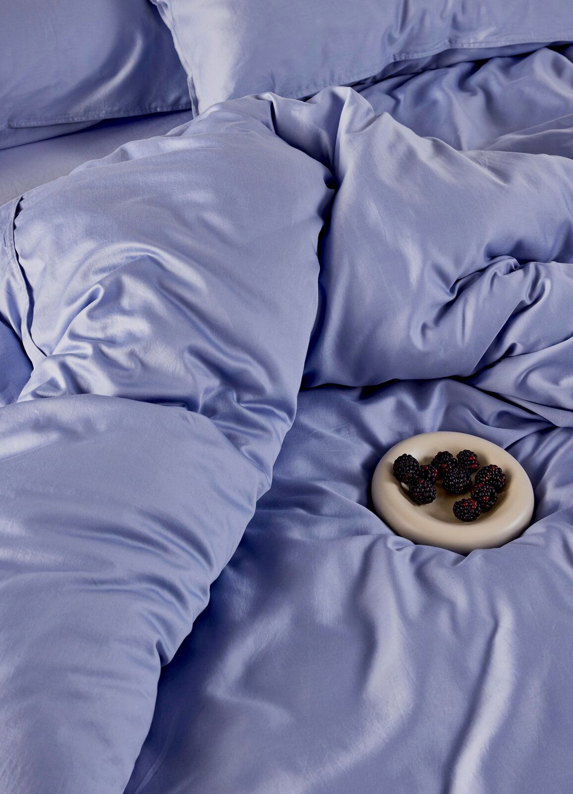 Blaue Bettwäsche aus der Vogelperspektive mit einem Teller Brombeeren.