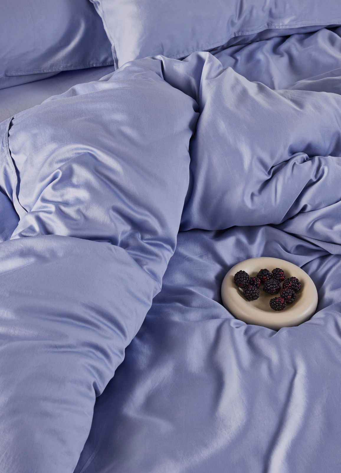 Blaue Bettwäsche aus der Vogelperspektive mit einem Teller Brombeeren.