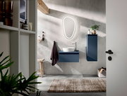 Moderne Badkombination mit blauem Waschtisch und Hängeschrank, beleuchtetem Spiegel und Waschbecken aus der Perspektive einer offenen Tür.