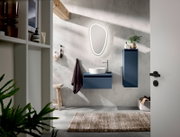 Moderne badkamercombinatie met blauwe wastafel en hangkast, verlichte spiegel en wastafel, gezien vanuit het perspectief van een open deur.
