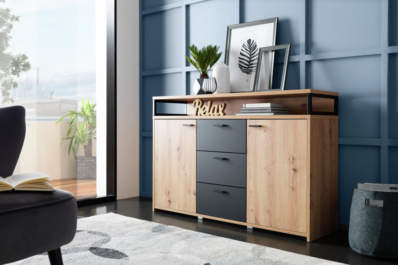 Modernes Sideboard aus Holz mit drei Schubladen und zwei Türen, dekoriert mit Pflanzen und Bildern, seitliche Perspektive.